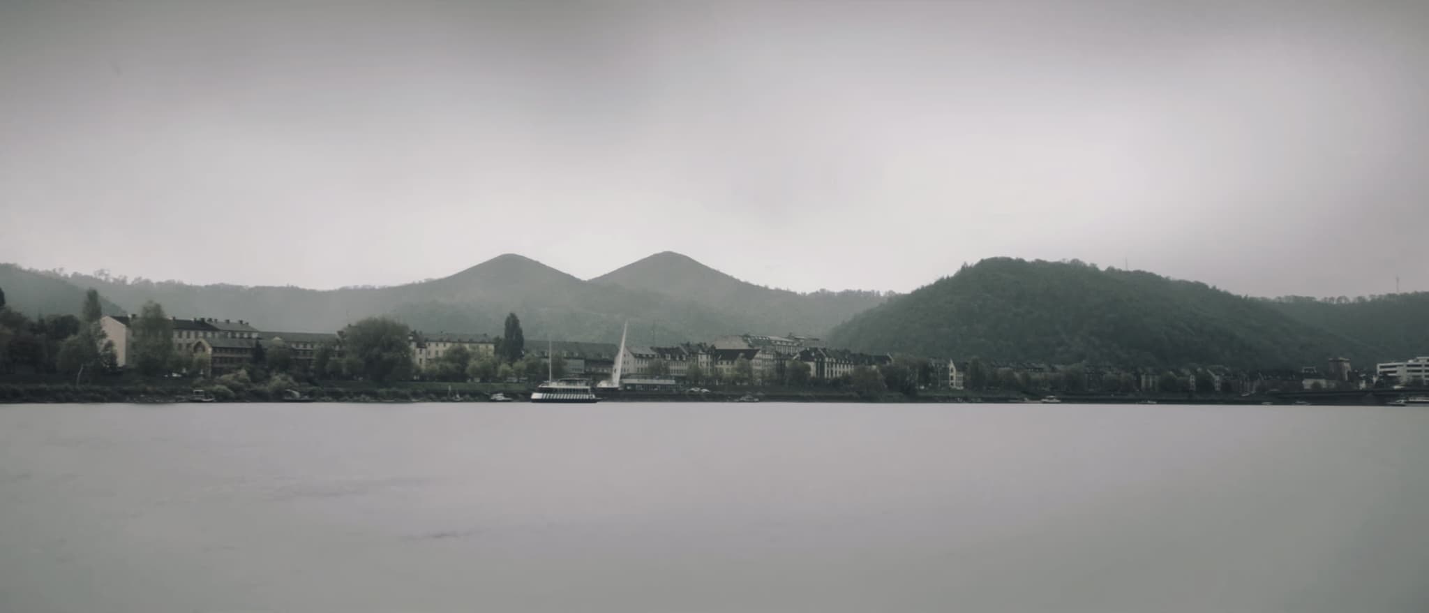 Der Rhein, die Stadt am Ufer, dahinter die runden Kuppen des Siebengebirges
