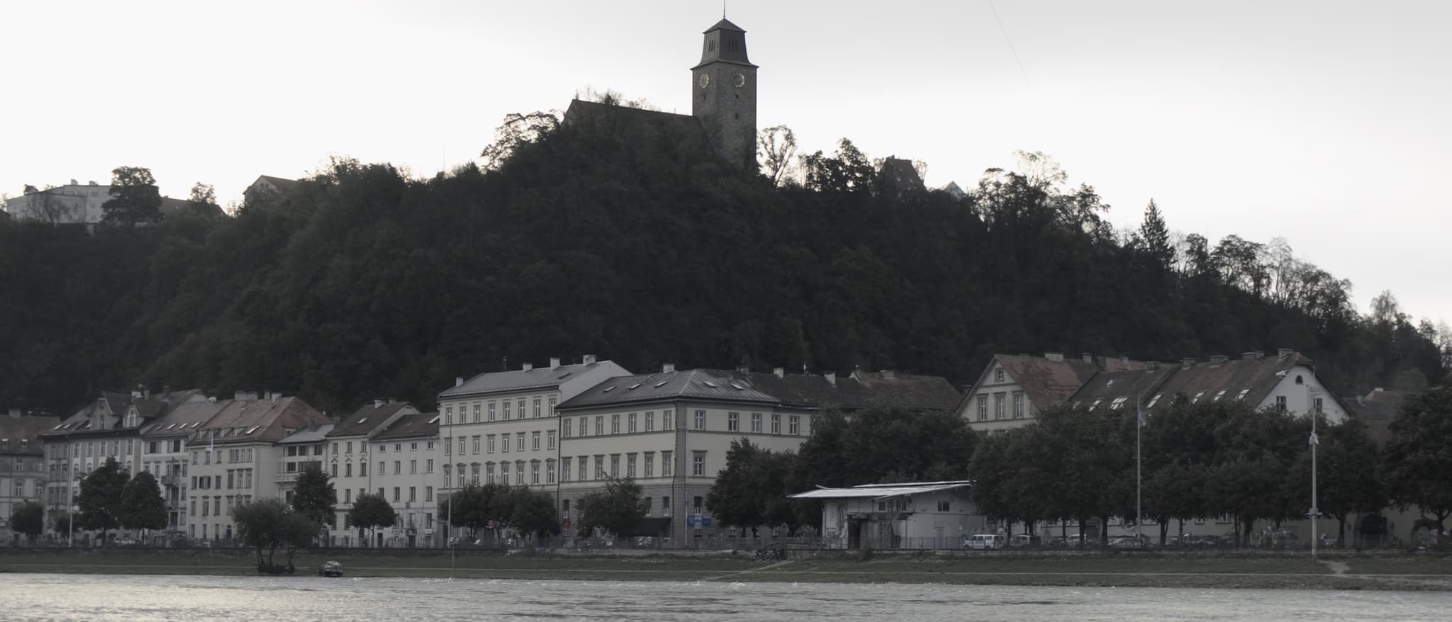 Der Fluss, ein bewaldeter Hügel über den Dächern, ein Uhrturm darauf
