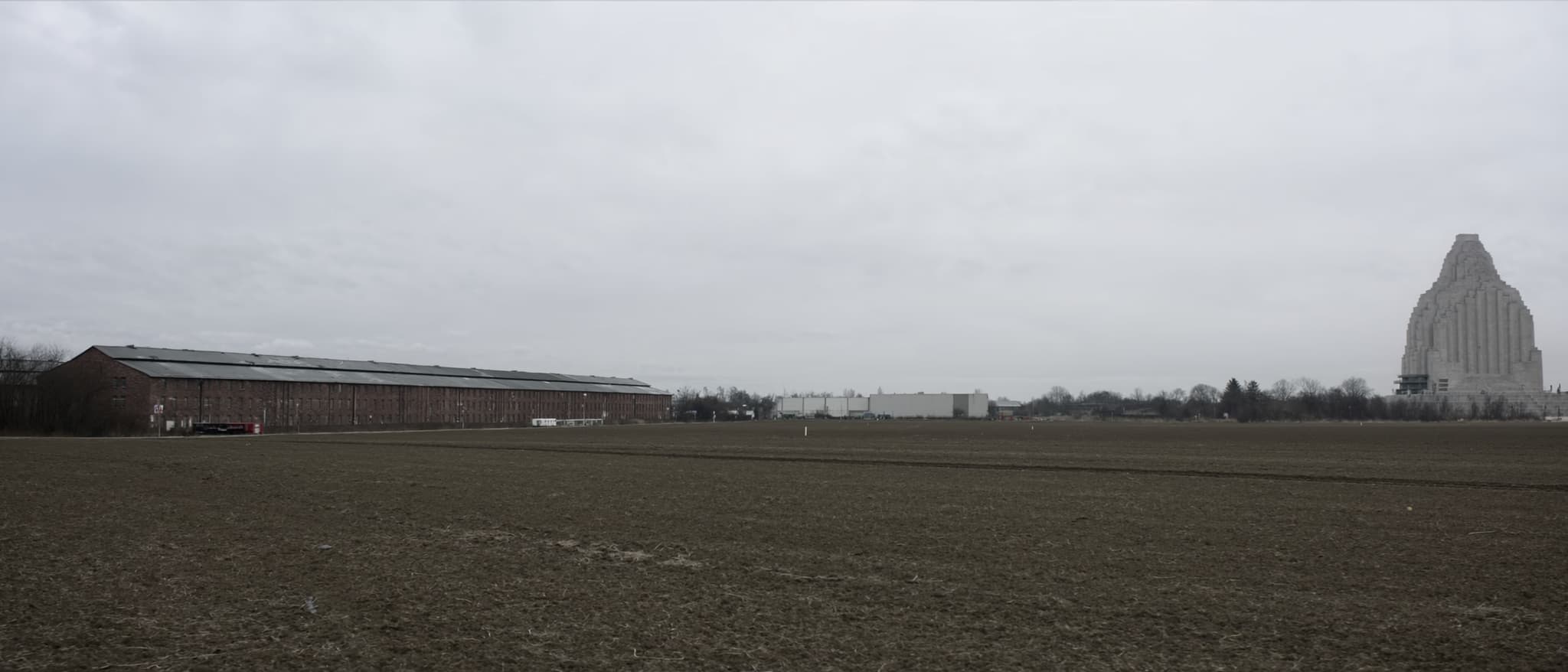 Eine lange Reihe Backsteinspeicher, dahinter ein Steinmonument im Dunst