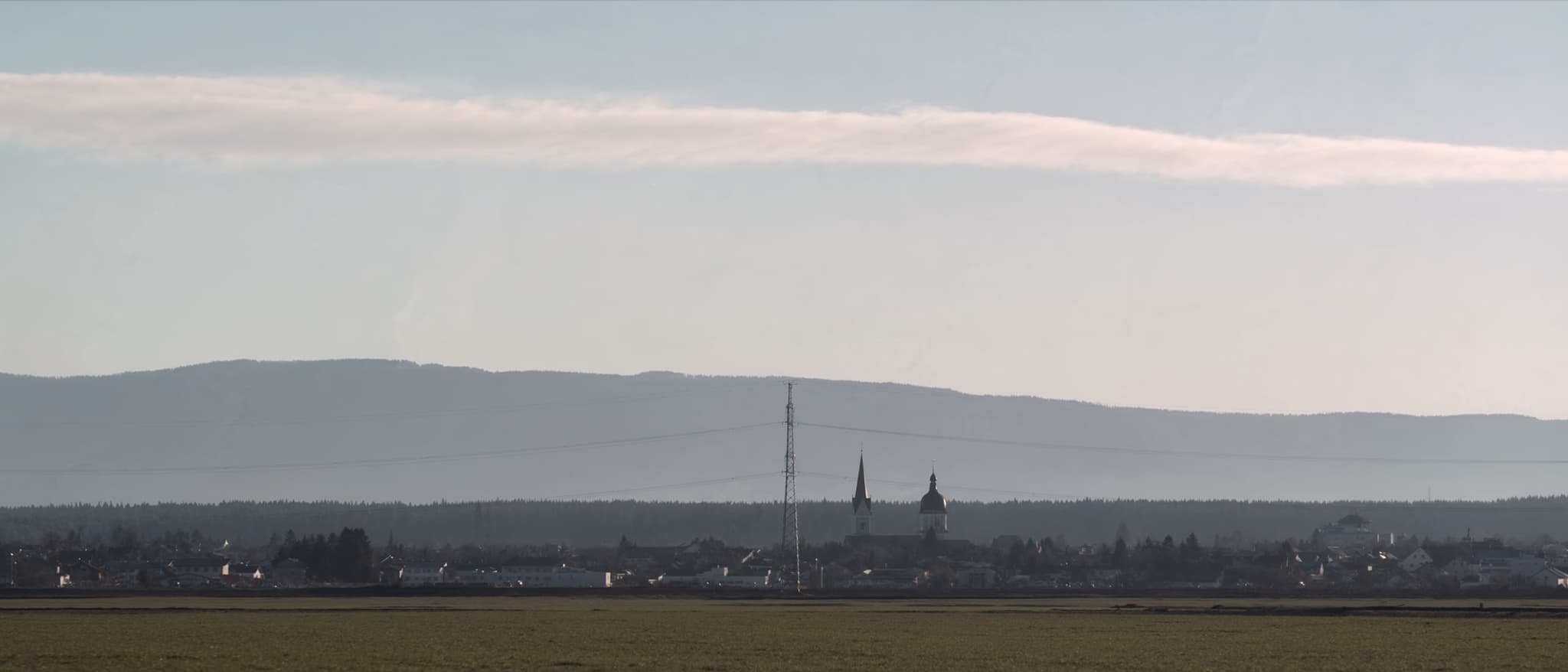 Flaches Land, eine Ortschaft, und dahinter die Kette der Voralpen