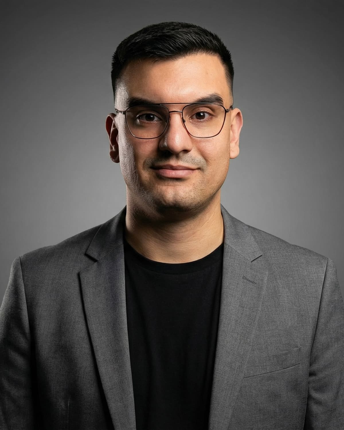 Damjan Savić, frontales Studioporträt vor grauem Hintergrund, graues Sakko über schwarzem Shirt